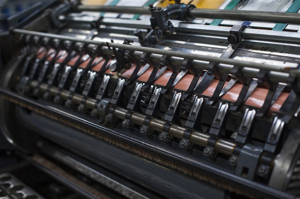 Close-up of paper stock feeding through a printing press, showing the sheet transport mechanism and impression cylinder.