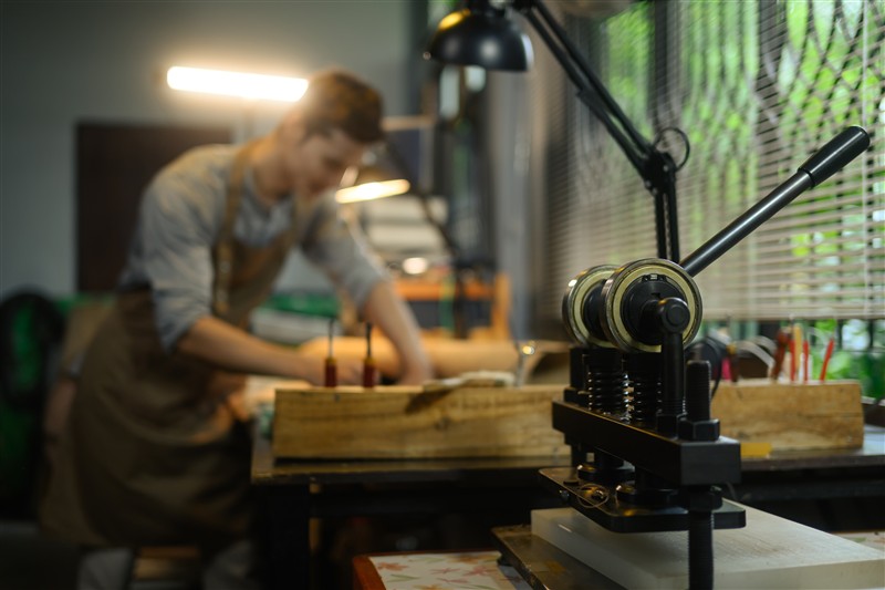 An old special press machine on a wooden table in a traditional workshop, representing the heritage craftsmanship of a long-established printing firm.