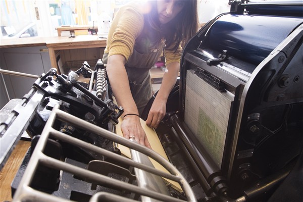 A woman preparing a printer in a workshop, calibrating the machine for a production run.